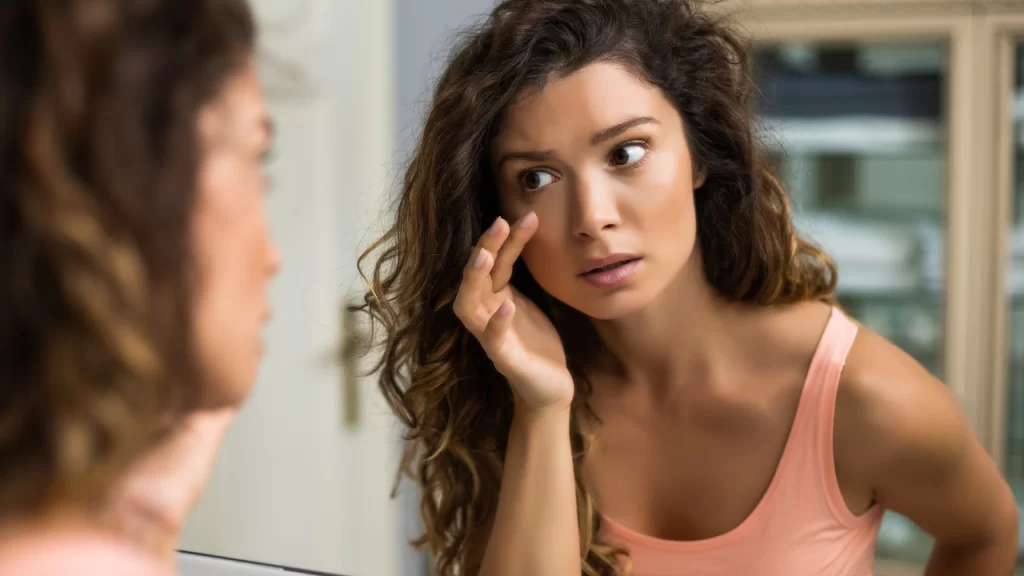 Image of woman looking at eyebags in the mirror